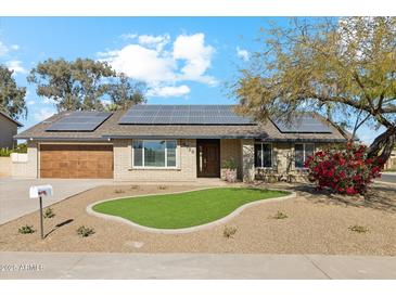 Single story home with solar panels, landscaped lawn, and a two-car garage at 4726 E Grandview Rd, Phoenix, AZ 85032