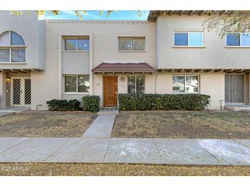 Tan two-story stucco townhome with a brown door and landscaping at 225 N Standage -- # 77, Mesa, AZ 85201