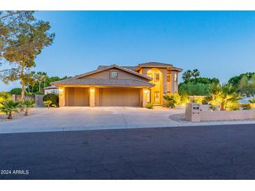 Two-story home featuring a circular driveway, a manicured lawn, desert landscaping and warm exterior lighting at 12015 S Tuzigoot Dr, Phoenix, AZ 85044