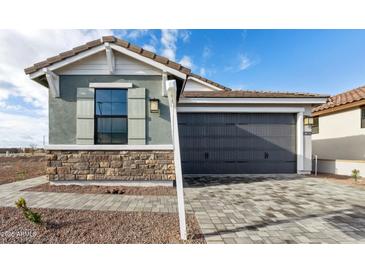 Charming home featuring a gray two-car garage, stone accents, and a beautifully paved driveway at 4380 N 203Rd Dr, Buckeye, AZ 85396