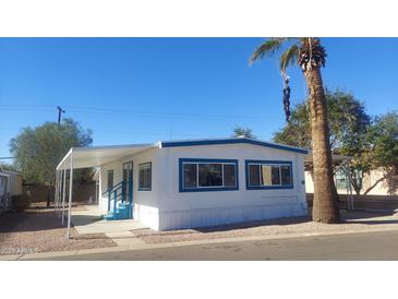 White single-wide mobile home with blue trim, covered carport, and desert landscaping at 201 S Greenfield Rd # 16, Mesa, AZ 85206