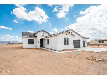 Inviting white stucco home featuring a three-car garage and desert landscape at 25505 W Brookhart Way, Wittmann, AZ 85361