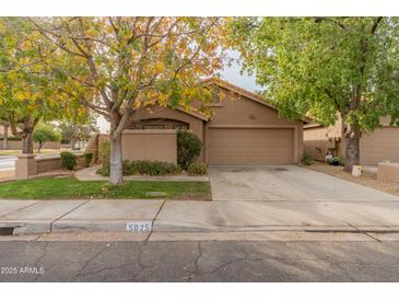 Tan house with a two-car garage and mature trees in the front yard at 5025 E Waltann Ln, Scottsdale, AZ 85254