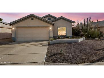 Charming single-story home featuring a two-car garage, desert landscaping, and warm exterior lighting at 14033 W Two Guns Trl, Surprise, AZ 85374