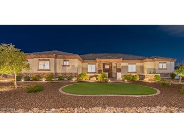 Inviting single-story home with a well-manicured lawn and decorative rock landscaping illuminated at night at 18206 W Solano Ct, Litchfield Park, AZ 85340