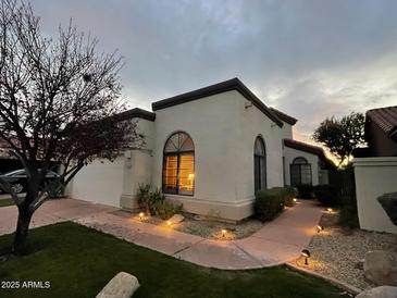 Charming home featuring a light stucco exterior, arched windows, and a meticulously landscaped yard with pathway lighting at 8243 E Cortez Dr, Scottsdale, AZ 85260