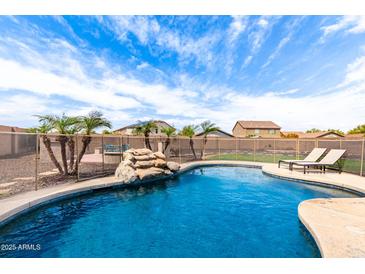 Inviting in-ground pool with rock waterfall feature, lounge chairs, and safety fence under a sunny, partly cloudy sky at 32504 N Cherry Creek Rd, San Tan Valley, AZ 85144