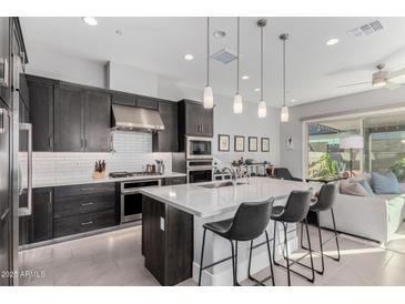 A modern kitchen boasts sleek, dark cabinetry, stainless steel appliances, and a large island with stylish pendant lighting at 25311 N 19Th Ln, Phoenix, AZ 85085