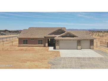 Single-story home with desert landscaping, neutral toned exterior, and a three-car garage in a fenced lot at 22270 W Skinner Rd, Wittmann, AZ 85361