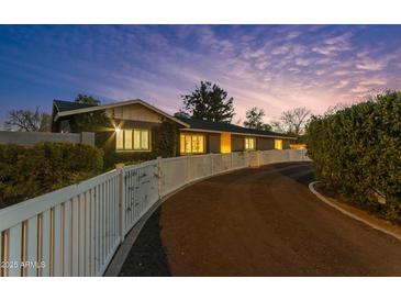 A winding driveway leads to this home that features a quaint white fence and mature landscaping at twilight at 5249 E Thunderbird Rd, Scottsdale, AZ 85254