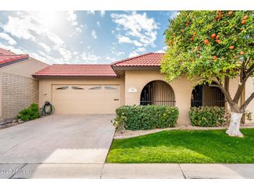 Tan stucco house with a tiled roof, attached garage, and lush landscaping at 7837 E Crestwood Way, Scottsdale, AZ 85250