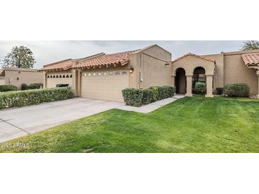 Tan stucco house with tile roof, two-car garage, and well-manicured lawn at 9103 E Winchcomb Dr, Scottsdale, AZ 85260