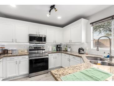 Bright kitchen features granite counters, stainless steel appliances, white cabinetry and recessed lighting at 222 S 223Rd Dr, Buckeye, AZ 85326