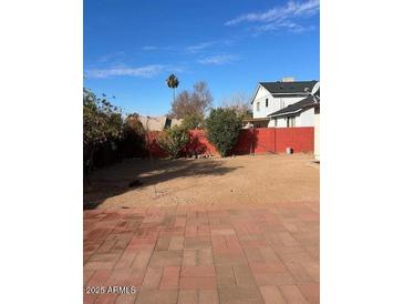 Large backyard featuring a brick-paved patio, gravel area, and a red fence under a bright blue sky at 4947 E Adobe St, Mesa, AZ 85205