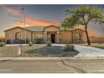 Charming single-story home with desert landscaping and a paved driveway, set against a dramatic sunset sky at 22717 W Sierra Ridge Way, Wittmann, AZ 85361