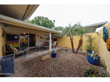 Cozy back patio with desert landscaping, covered area with chairs, and sliding glass doors to interior at 10407 N 108Th Ave, Sun City, AZ 85351