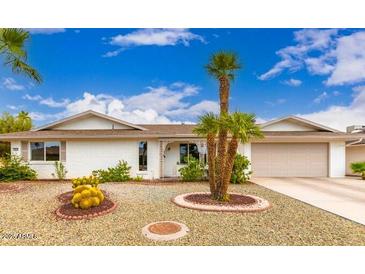 Charming single-story home featuring a desert-style front yard with palm trees under a bright blue sky at 12415 W Rock Springs Dr, Sun City West, AZ 85375