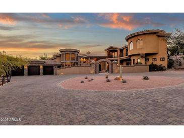 Stunning home exterior with circular driveway, desert landscaping, and stone accents beneath a vibrant sunset sky at 9815 N Copper Ridge Trl, Fountain Hills, AZ 85268