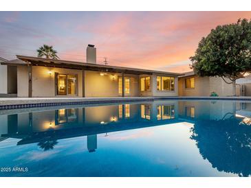 Backyard pool reflecting the house at dusk with a covered patio and lush foliage at 302 E Coral Gables Dr, Phoenix, AZ 85022