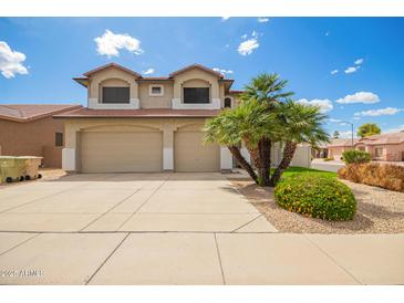 Two-story tan home featuring a three-car garage, desert landscaping, and a red tile roof at 19520 N 65Th Ave, Glendale, AZ 85308
