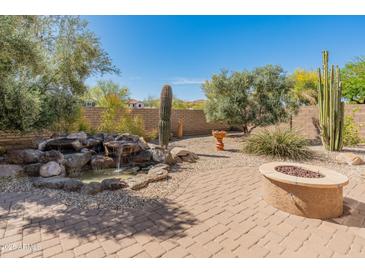 Lush backyard oasis with a rock waterfall feature, fire pit, and desert landscaping at 12541 W Miner Trl, Peoria, AZ 85383