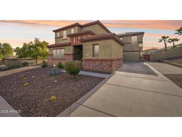 Two-story home featuring desert landscaping, red stone accents, and a long driveway at 12017 W Monte Lindo Ln, Sun City, AZ 85373