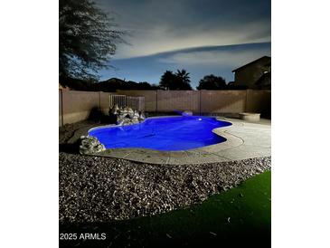 Inviting in-ground pool with rock waterfall feature, surrounded by mature landscaping and a cozy firepit area for outdoor relaxation at 2212 W Alicia Dr, Phoenix, AZ 85041