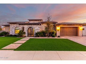 Elegant stone home featuring an arched entry gate, manicured lawn, and attached two car garage at 2799 E Waterman St, Gilbert, AZ 85297