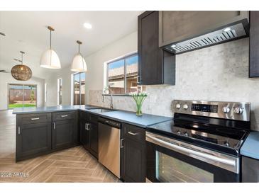 Well-lit kitchen featuring stainless steel appliances, dark cabinets, light backsplash, and modern pendant lighting at 21824 N 32Nd Ave, Phoenix, AZ 85027