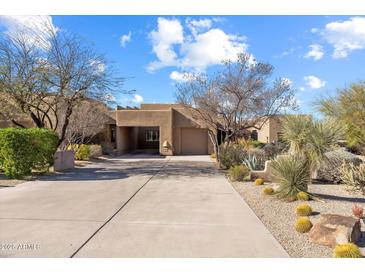 Desert landscaping enhances the front of this single-story home with neutral exterior and a large driveway at 9221 E Whitethorn Cir, Scottsdale, AZ 85266