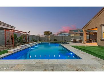 Stunning backyard pool with waterfalls, travertine tile, artificial turf and outdoor seating at twilight at 41954 W Plata St, Maricopa, AZ 85138