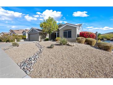 Charming single-story home with desert landscaping, rock stream, and mature tree on a sunny day at 104 W Windsong Dr, Phoenix, AZ 85045