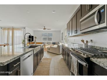 Modern kitchen featuring granite countertops, stainless steel appliances, and a view into the adjacent living room at 35250 W Merced St, Maricopa, AZ 85138