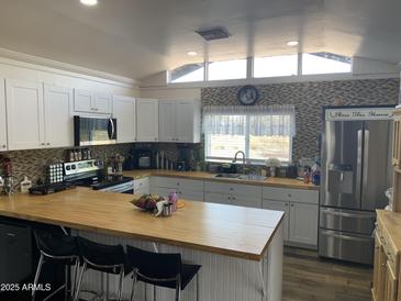 Bright kitchen featuring white cabinets, butcher block countertops, mosaic backsplash, and stainless steel appliances at 32628 N 163Rd Ave, Surprise, AZ 85387