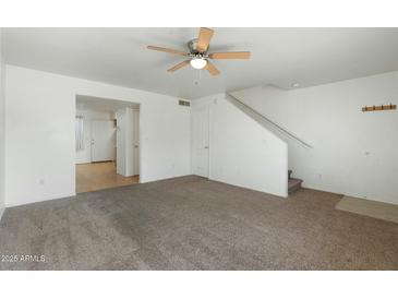Bright living room with neutral carpet, ceiling fan, and staircase to the upper level at 18239 N 40Th St # 107, Phoenix, AZ 85032