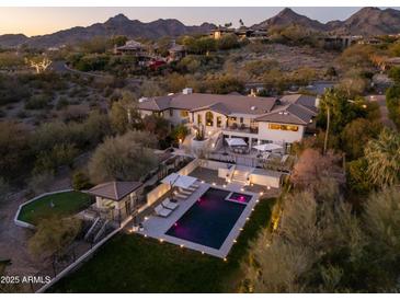 Stunning aerial view of a luxury home with pool, lush landscaping, and mountain backdrop at dusk at 3977 E Paradise View Dr, Paradise Valley, AZ 85253