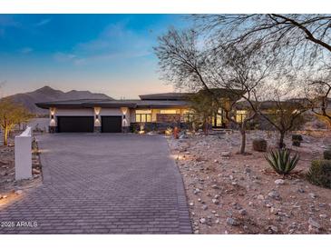 A luxury home featuring a stone facade, a brick driveway, desert landscaping, and a mountain backdrop at 3744 N Rock Wren Ct, Buckeye, AZ 85396