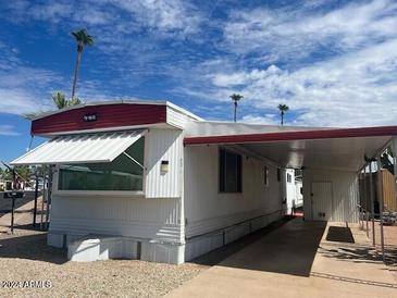 Cozy mobile home featuring white siding, red trim, awning, and carport for convenient parking at 4065 E University Dr # 271, Mesa, AZ 85205