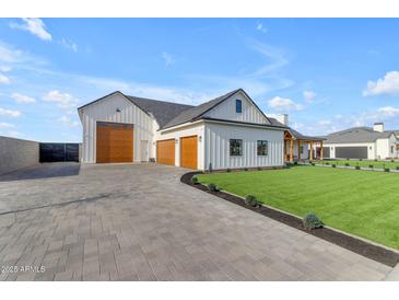 Stunning white farmhouse with wood garage doors and a paved driveway surrounded by manicured landscaping at 2312 N Raven --, Mesa, AZ 85207