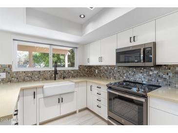 Modern kitchen featuring white cabinets, mosaic backsplash, stainless steel appliances, and a farmhouse sink under the window at 4220 E Everett Dr, Phoenix, AZ 85032