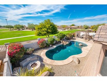 An aerial view of a kidney-shaped pool, fire pit, and surrounding landscape with a golf course in the background at 4488 N 155Th Ave, Goodyear, AZ 85395