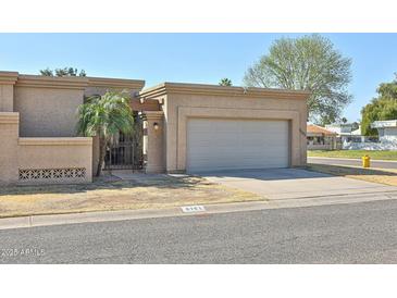 Tan home with a two-car garage, well-maintained yard, and a security gate at 8151 E Del Joya Dr, Scottsdale, AZ 85258