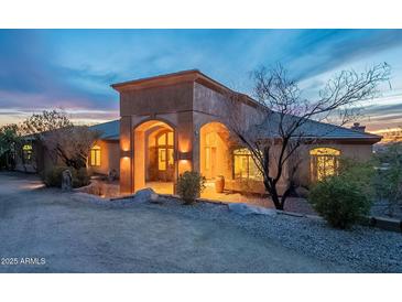 Stunning exterior shot of a home with unique architectural features, beautiful desert landscaping, and warm lighting at dusk at 3086 N Herrala Way, Apache Junction, AZ 85119