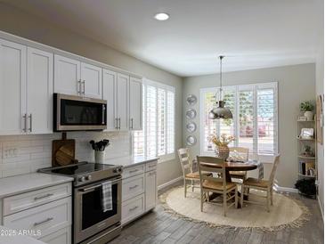 Bright kitchen featuring stainless steel appliances, white cabinetry, and a cozy dining area with shuttered windows at 20315 N 82Nd Ln, Peoria, AZ 85382