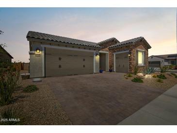 Charming home featuring a two-car garage, stone accents, landscaped yard, and a paved driveway at 27366 W Escuda Dr, Buckeye, AZ 85396