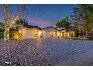 Beautiful home exterior with a long driveway, mature trees, and three-car garage, set against a twilight sky at 5020 E Pershing Ave, Scottsdale, AZ 85254