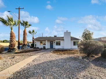 Charming single-story home with a blue door and white exterior, complemented by desert landscaping and palm trees at 701 W Wilshire Dr, Phoenix, AZ 85007