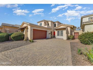 Inviting exterior with a paver driveway, two-car garage, and well-maintained landscaping under a bright blue sky at 14561 W Hidden Terrace Loop, Litchfield Park, AZ 85340