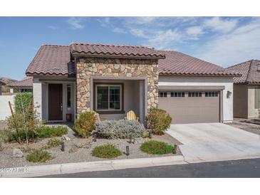 Inviting single-story home with stone accents, desert landscaping, and a charming covered porch and tile roof at 20392 W Brittlewood Ave, Buckeye, AZ 85396