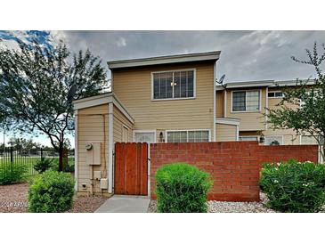 Tan townhouse with a red brick gate, trimmed shrubbery, and a healthy shade tree on a cloudy day at 625 S Westwood St # 108, Mesa, AZ 85210